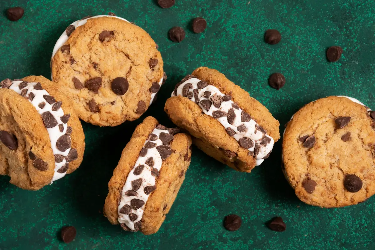 Chocolate chip cookie ice cream sandwiches with mini chocolate chips on a dark green background.