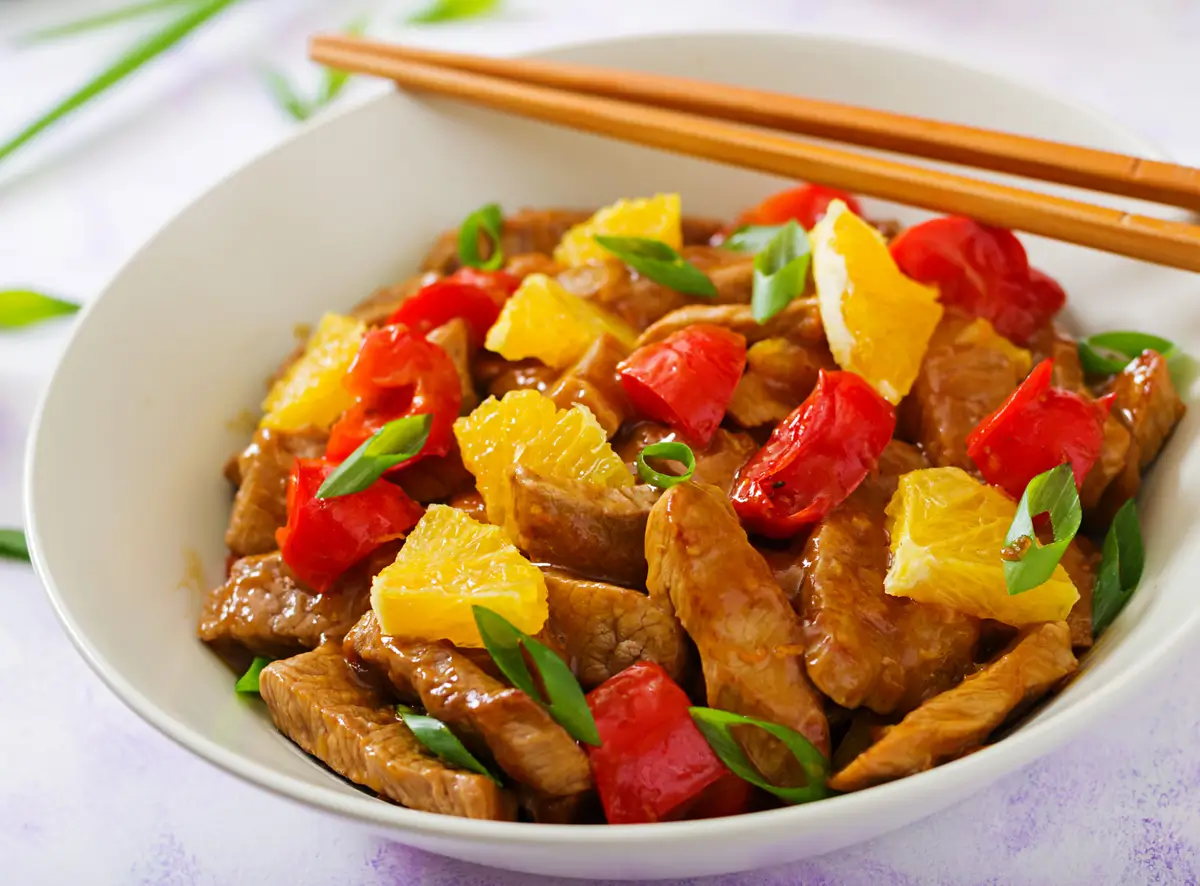 A bowl of black pepper chicken panda express garnished with peppers, sesame seeds, and green onions.