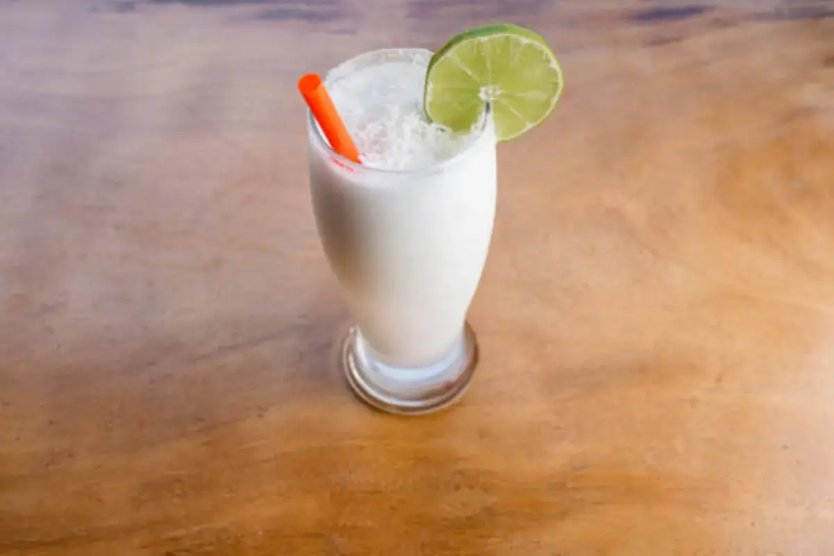 A creamy white cocktail garnished with a lime slice and served with a straw